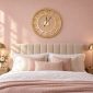 Gold openwork wall clock above a bed on a blush pink wall